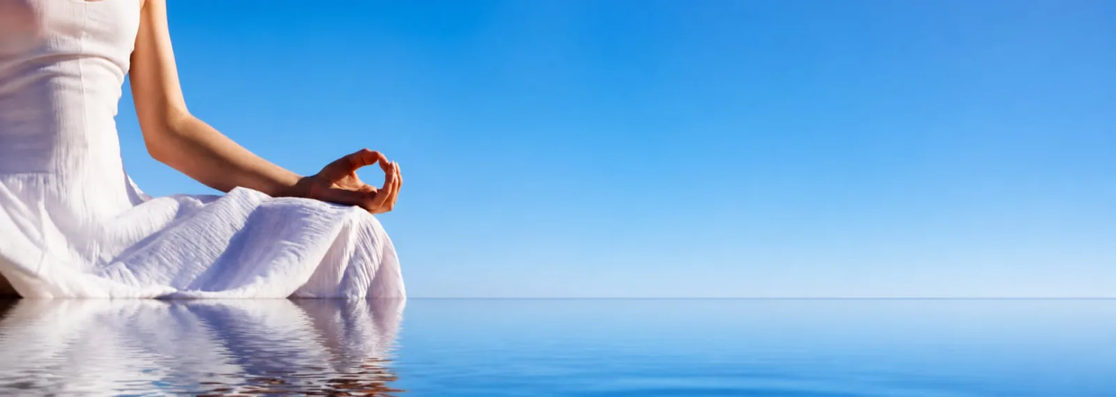 Persona vestida de blanco sentada en flor de loto, meditando frente a un horizonte de agua en calma y cielo azul